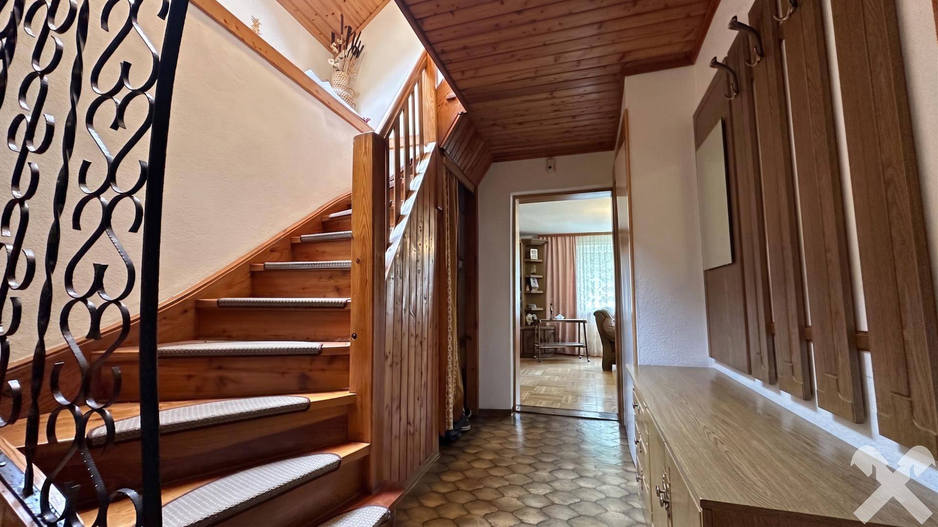 Geräumiger Flur mit Holztreppe, schmiedeeisernem Geländer und Holzvertäfelung an der Decke.