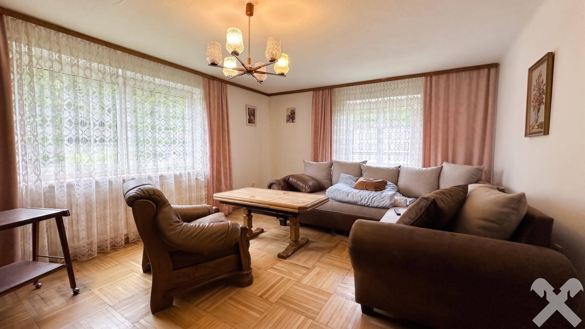 Helles Wohnzimmer mit Parkettboden, großen Fenstern und traditionellen Sitzmöbeln.