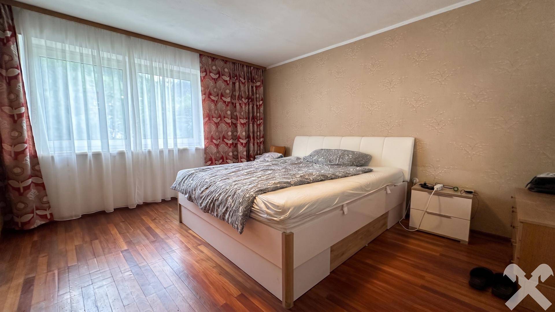 Schlafzimmer mit Holzboden, großem Bett und Fenster mit Blick ins Grüne.