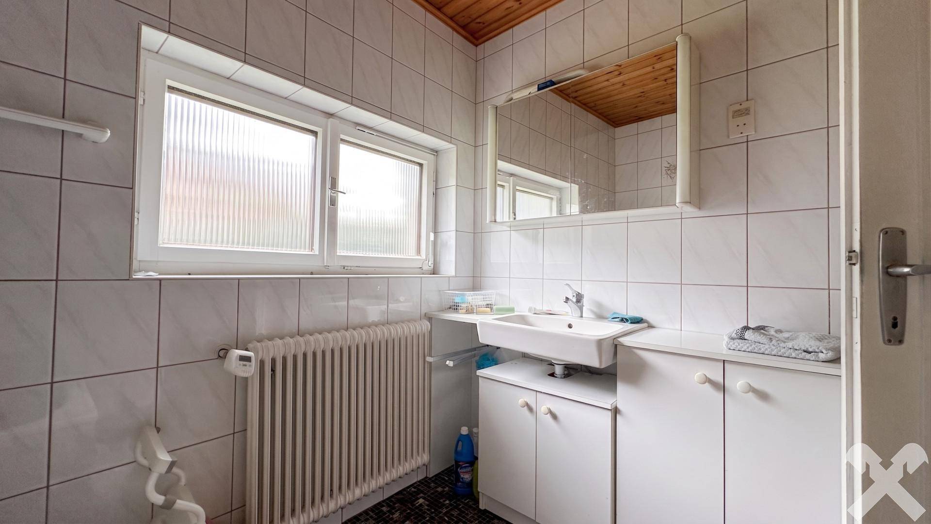 Badezimmer mit weißen Fliesen, Waschbecken und Fenster für Tageslicht.