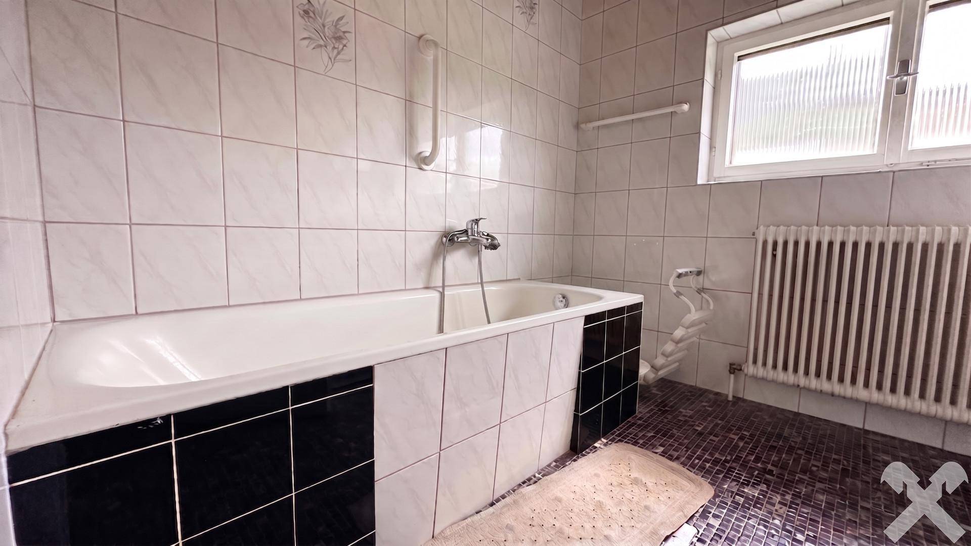 Badezimmer mit Badewanne, weißen Fliesen und Heizkörper unter dem Fenster.
