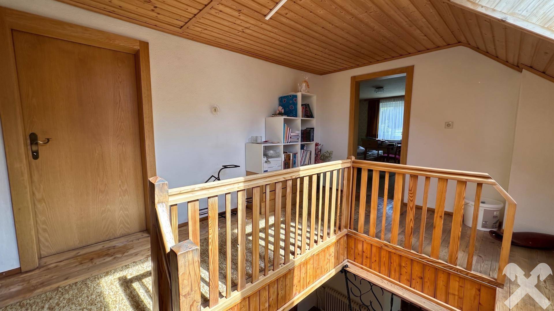 Obergeschoss-Flur mit Holzgeländer, Holzdecke und Zugang zu weiteren Räumen.