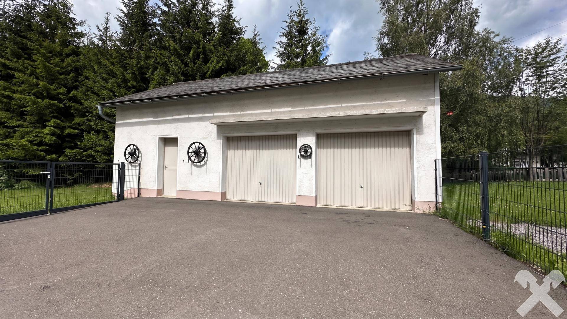 Doppelgarage mit zwei Toren und Zufahrt, umgeben von Grünflächen.