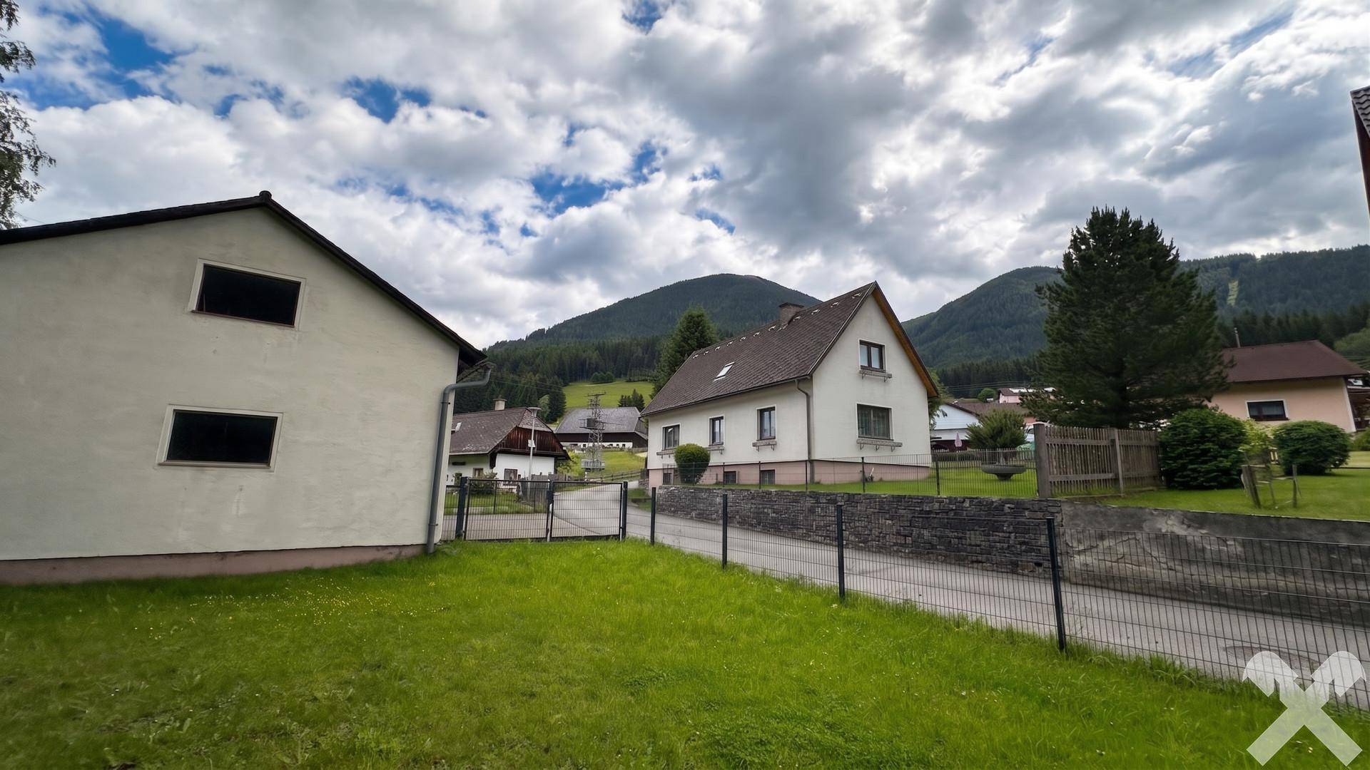 Gesamtansicht des Hauses und der Garage mit umliegender Natur und Bergblick.