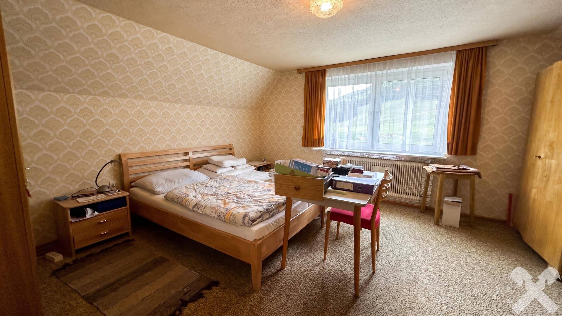 Schlafzimmer im Dachgeschoss mit Dachschräge, Holzbett und Blick ins Grüne.