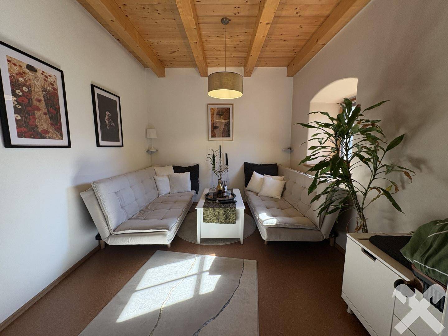 Gemütliches Wohnzimmer mit zwei Sofas, Couchtisch und rustikaler Holzbalkendecke.