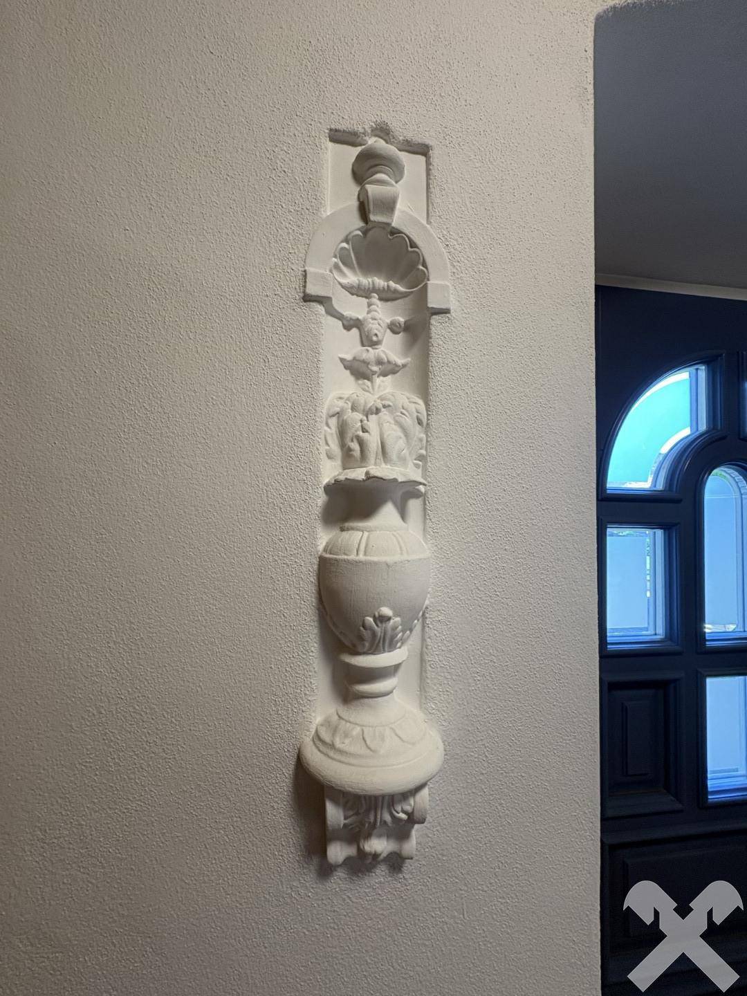 Detailaufnahme einer dekorativen Stuckverzierung an der Wand neben einem Türrahmen.