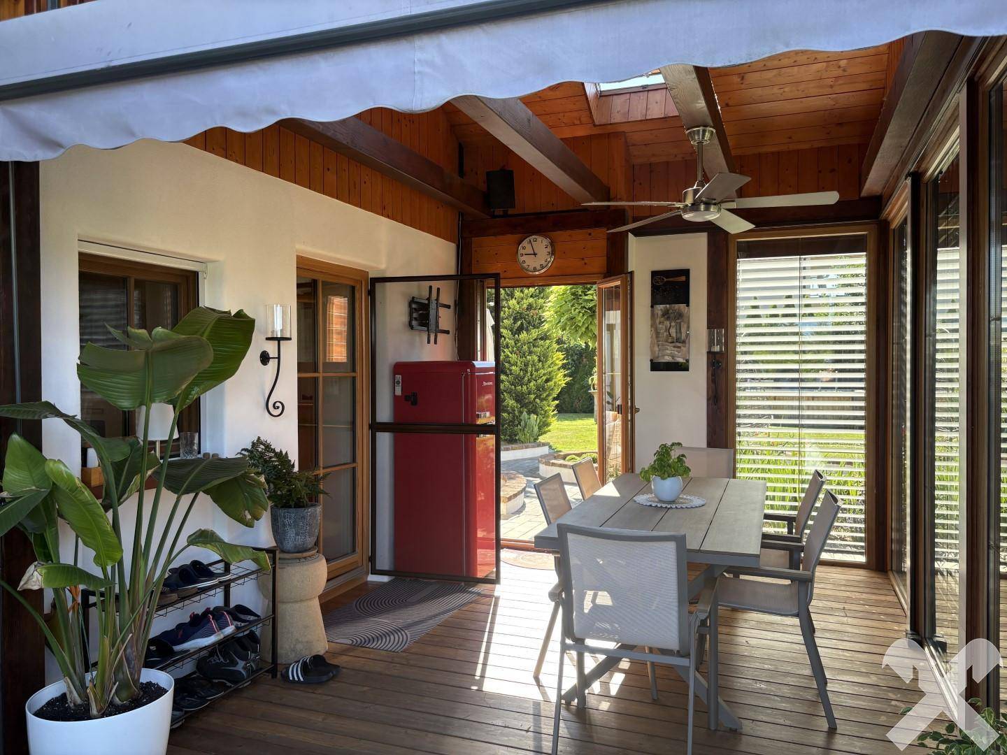 Überdachte Terrasse mit Esstisch, Deckenventilator und Zugang zum grünen Gartenbereich.