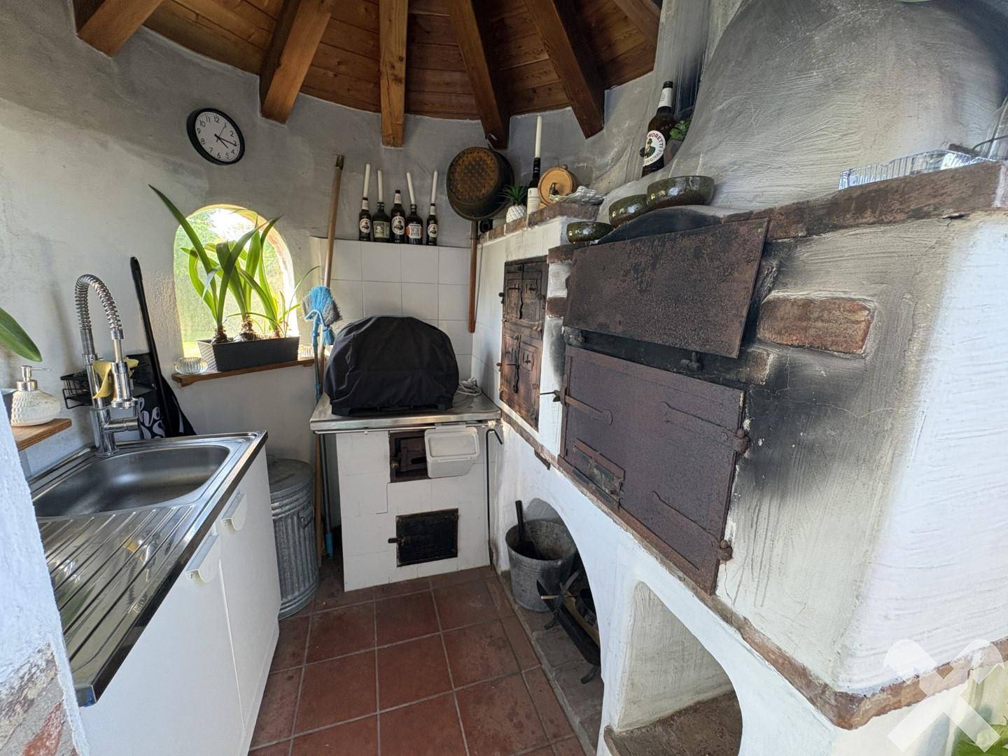 Rustikale Außenküche mit Spülbecken, traditionellem Holzofen und Terrakotta-Fliesenboden.