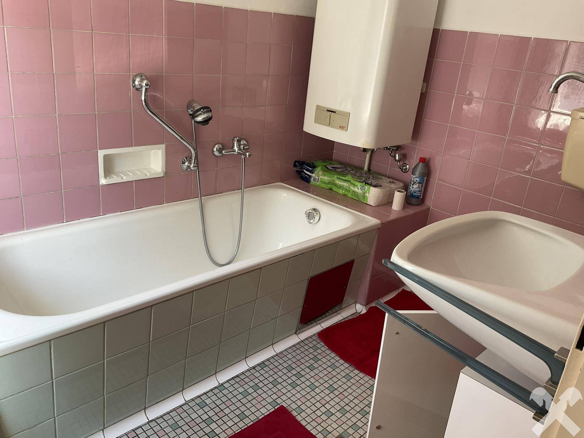 Badezimmer mit rosa Fliesen, einer Badewanne und einem Waschbecken im Stil der 80er Jahre.