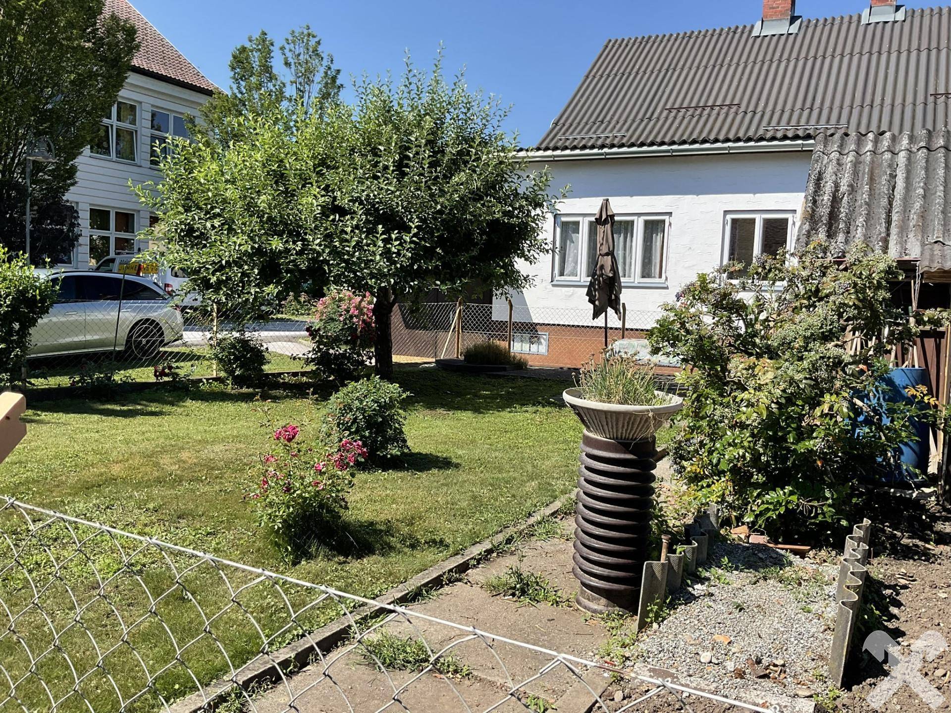 Gartenansicht mit weitläufiger Rasenfläche, Bäumen und einem dekorativen Pflanzgefäß.