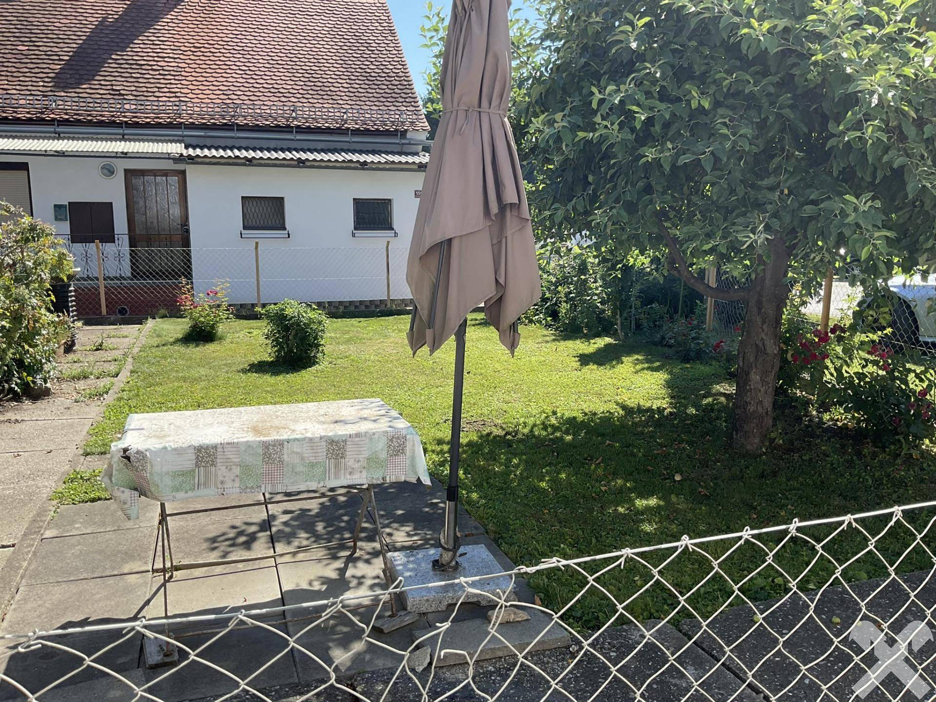 Weiterer Blick in den Garten mit Rasen, Obstbaum und einem Sonnenschirm über dem Tisch.