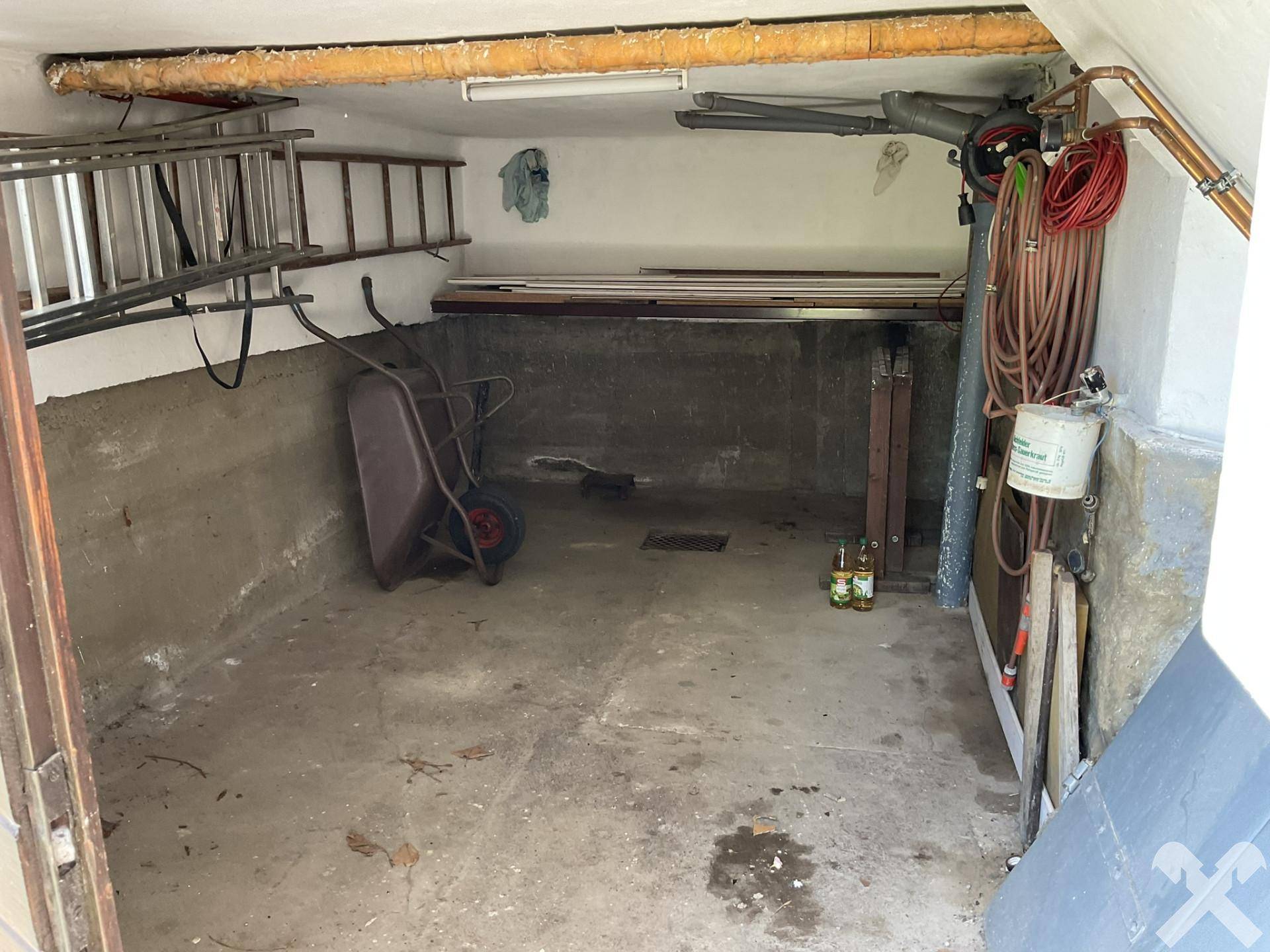 Geräumige Garage oder Abstellraum mit Betonboden, Werkzeugen und Leitern.