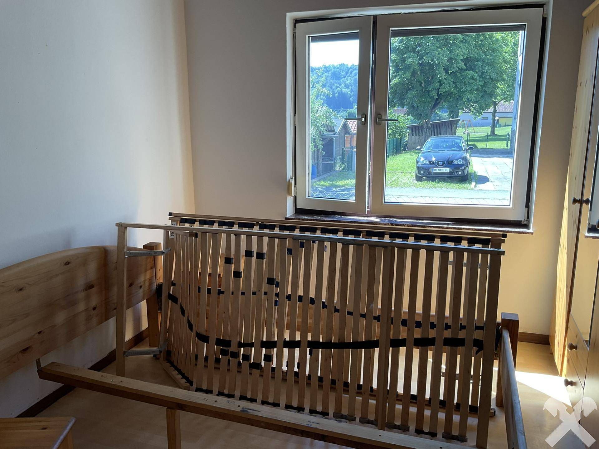 Schlafzimmer mit Fensterblick ins Grüne und einem zerlegten Bettgestell aus hellem Holz.