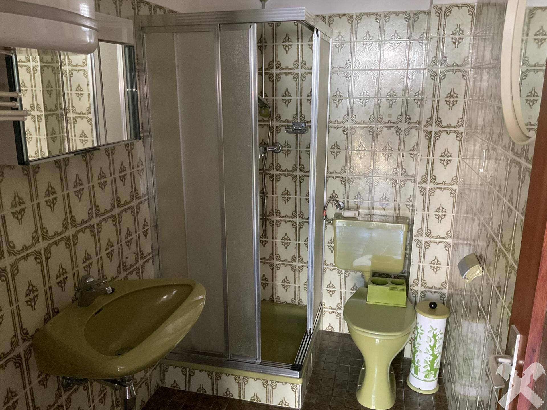 Badezimmer im Stil der 80er Jahre mit grünen Sanitärobjekten und gemusterten Fliesen.