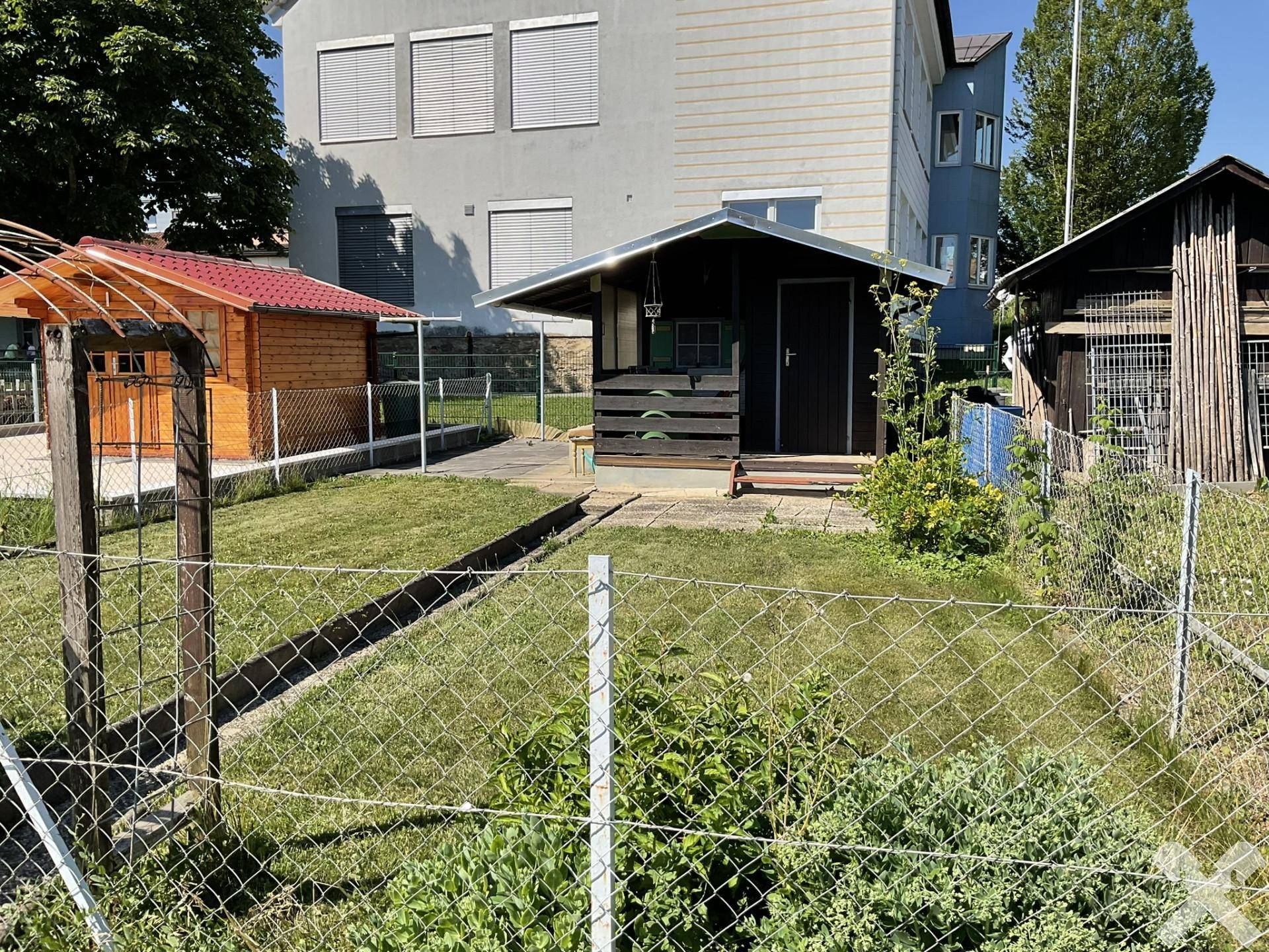 Gartenbereich mit zwei kleinen Gartenhäusern und Rasenfläche, umzäunt von einem Maschendrahtzaun.