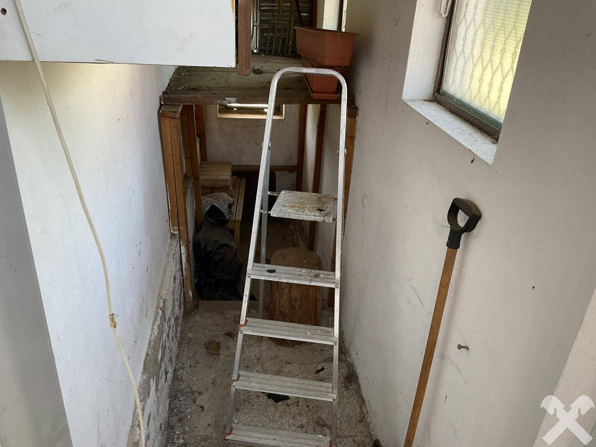 Treppenabgang in den Kellerbereich mit einer Leiter und sichtbaren Rohbau-Elementen.