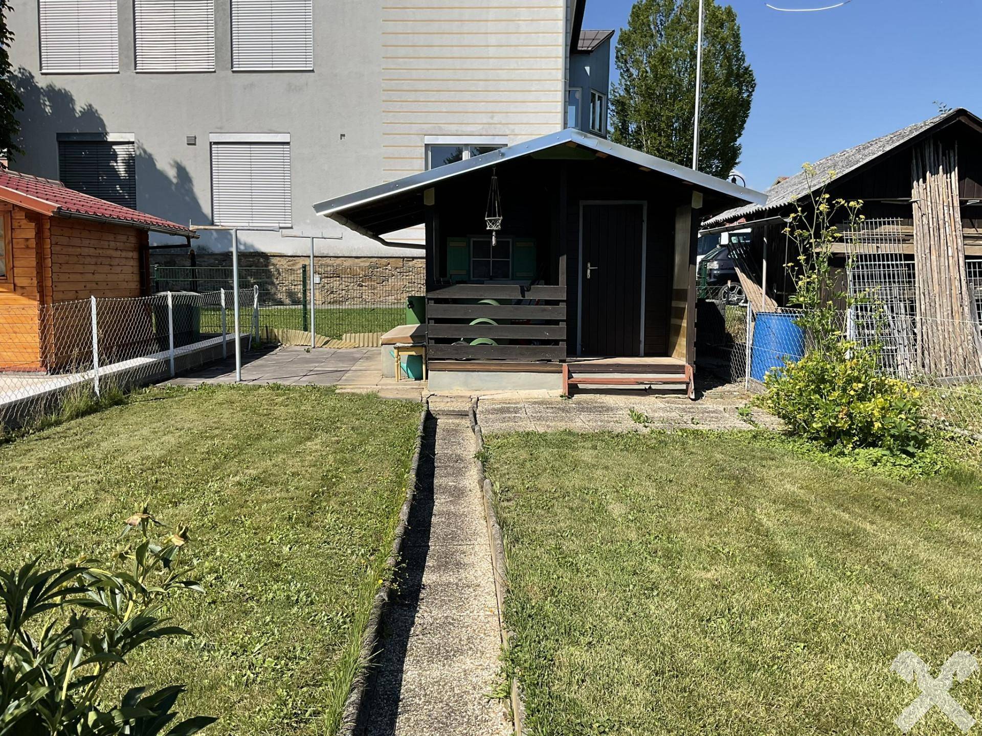 Gepflegter Garten mit Rasenfläche und einem Gartenhaus, umgeben von einem Zaun.
