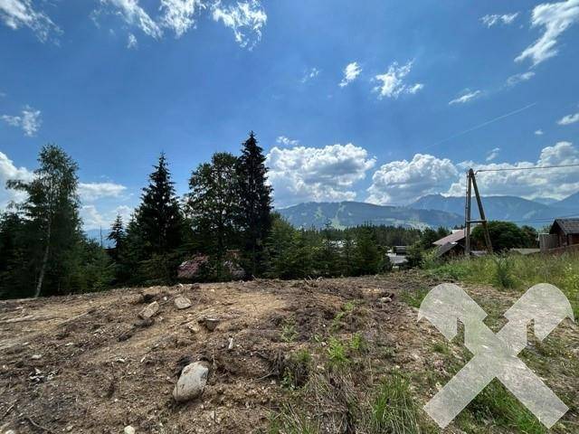 Freies Baugrundstück mit weitem Blick auf die umliegende Berglandschaft unter blauem Himmel.