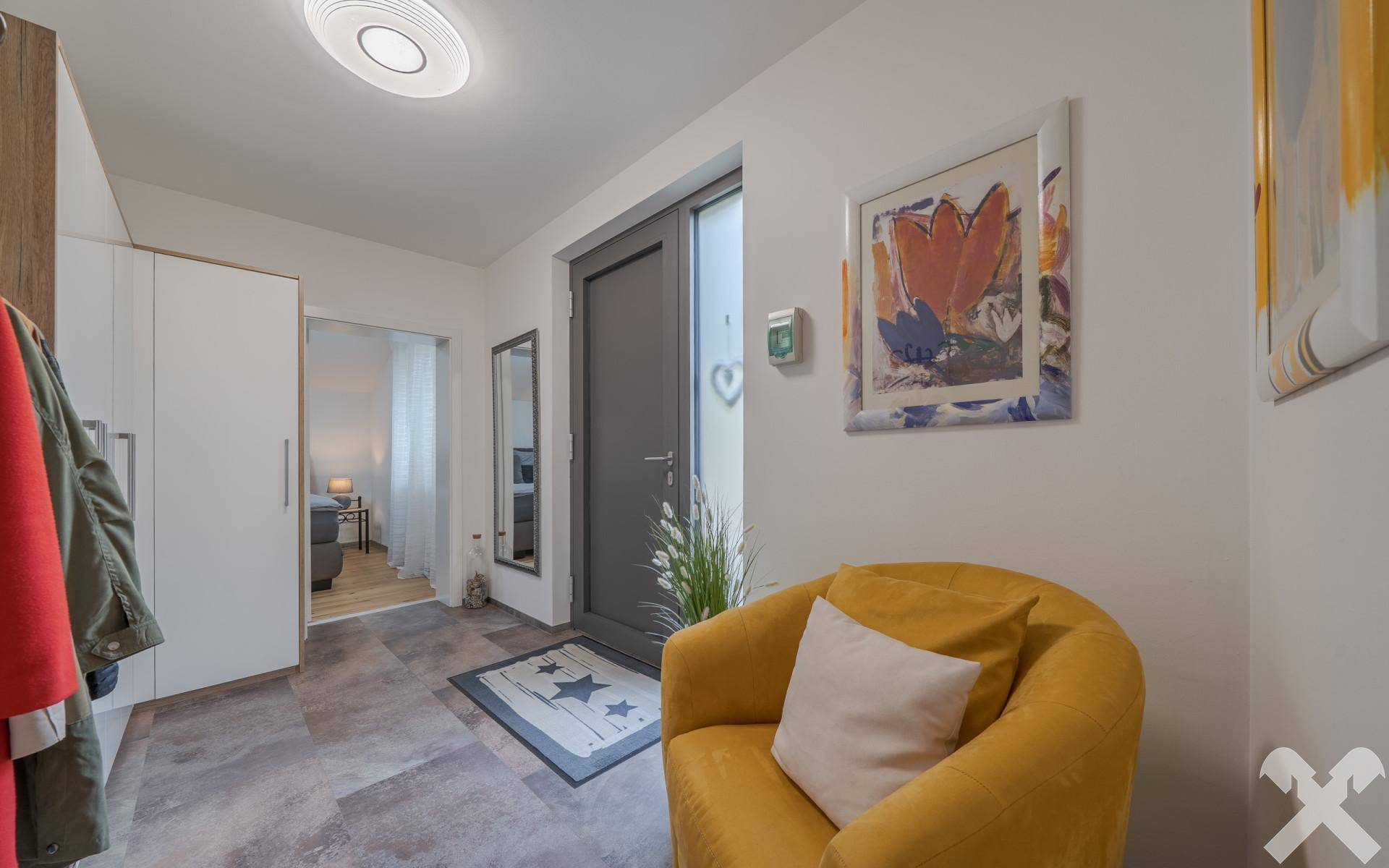 Heller Eingangsbereich mit Garderobe, moderner Einrichtung und einem bequemen gelben Sessel.