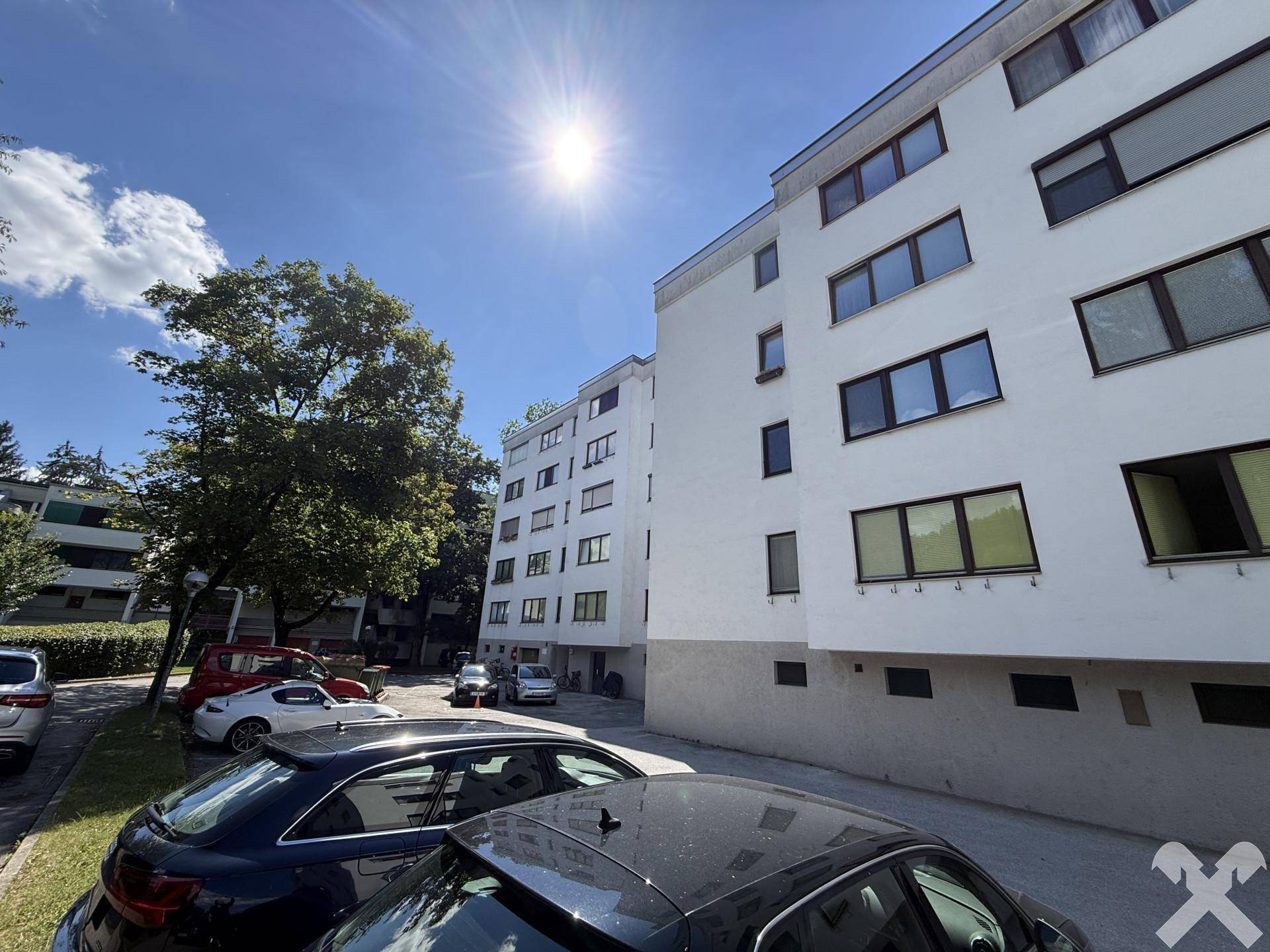 Modernes Mehrfamilienhaus mit weißer Fassade und Parkplätzen im Vordergrund an einem sonnigen Tag.