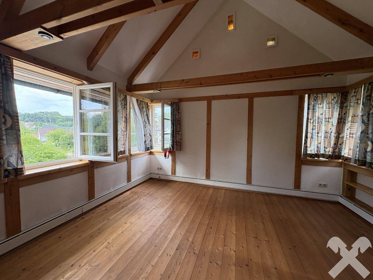 Helles Schlafzimmer mit Holzboden, sichtbaren Balken und mehreren Fenstern mit Ausblick.
