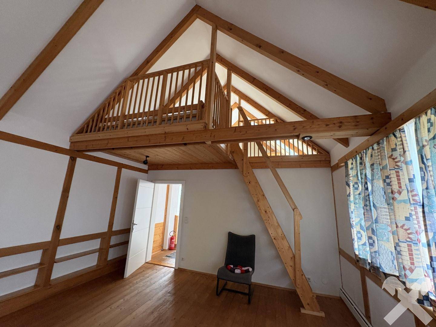 Geräumiger Raum im Dachgeschoss mit Holzbalken, Holztreppe und einem erhöhten Schlafbereich.