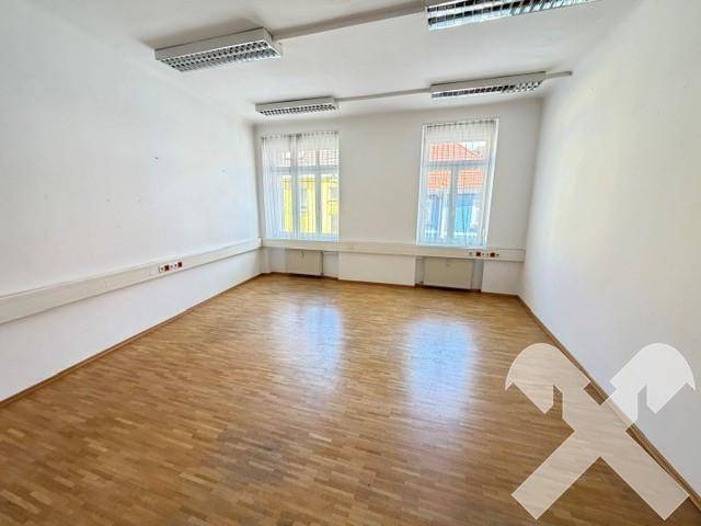 Heller Büroraum mit Holzboden, zwei großen Fenstern und Deckenbeleuchtung.