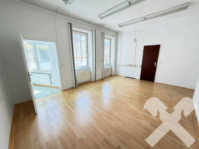 Heller Büroraum mit Holzboden, großen Fenstern und einer braunen Tür.