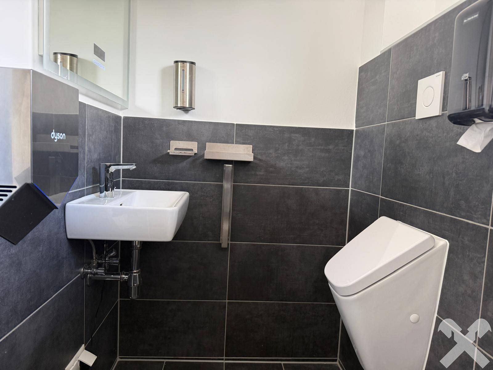 Modernes Gäste-WC mit dunklen Fliesen, Urinal und wandhängendem Waschbecken.
