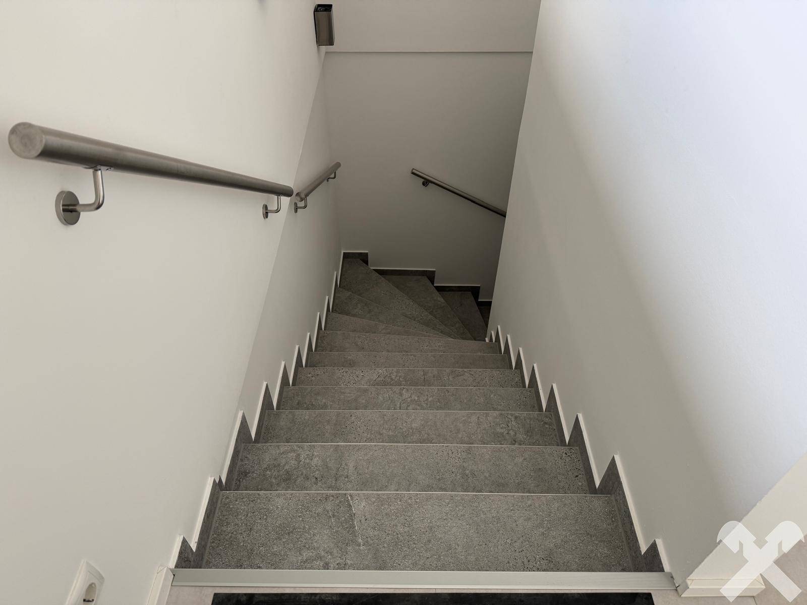 Moderne Treppe mit Fliesenstufen und Edelstahlgeländer, die in die oberen Etagen führt.