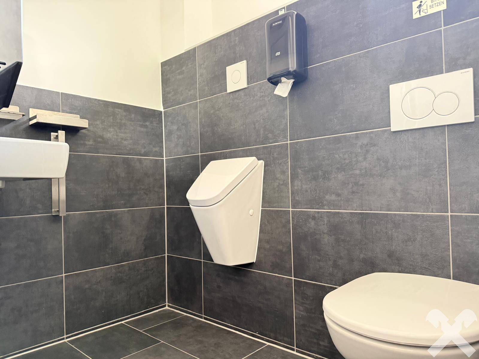 Modernes Gäste-WC mit dunklen Fliesen, Urinal und wandhängender Toilette.