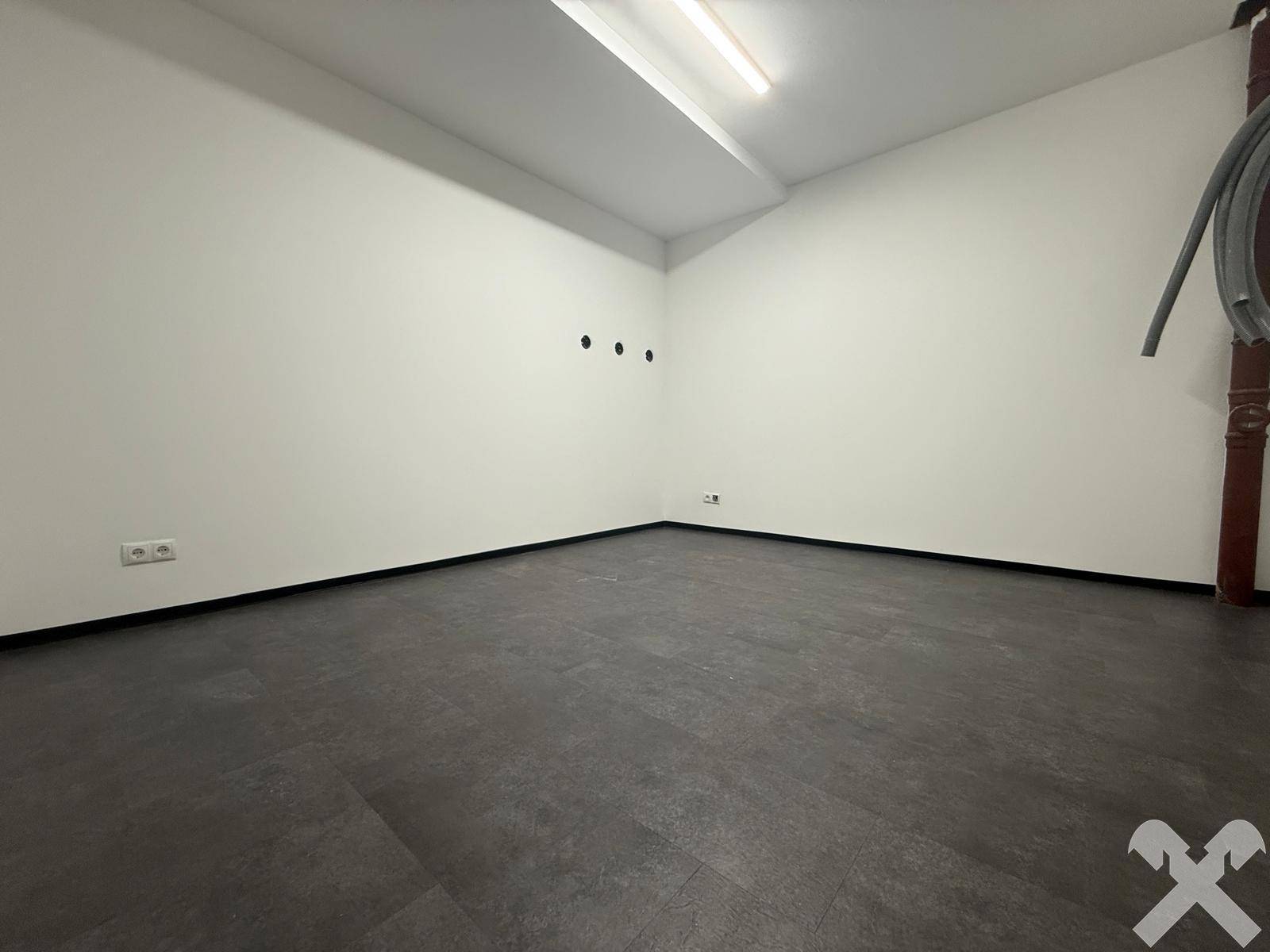 Leerer Raum mit dunklem Fliesenboden und weißen Wänden, vielseitig nutzbar.