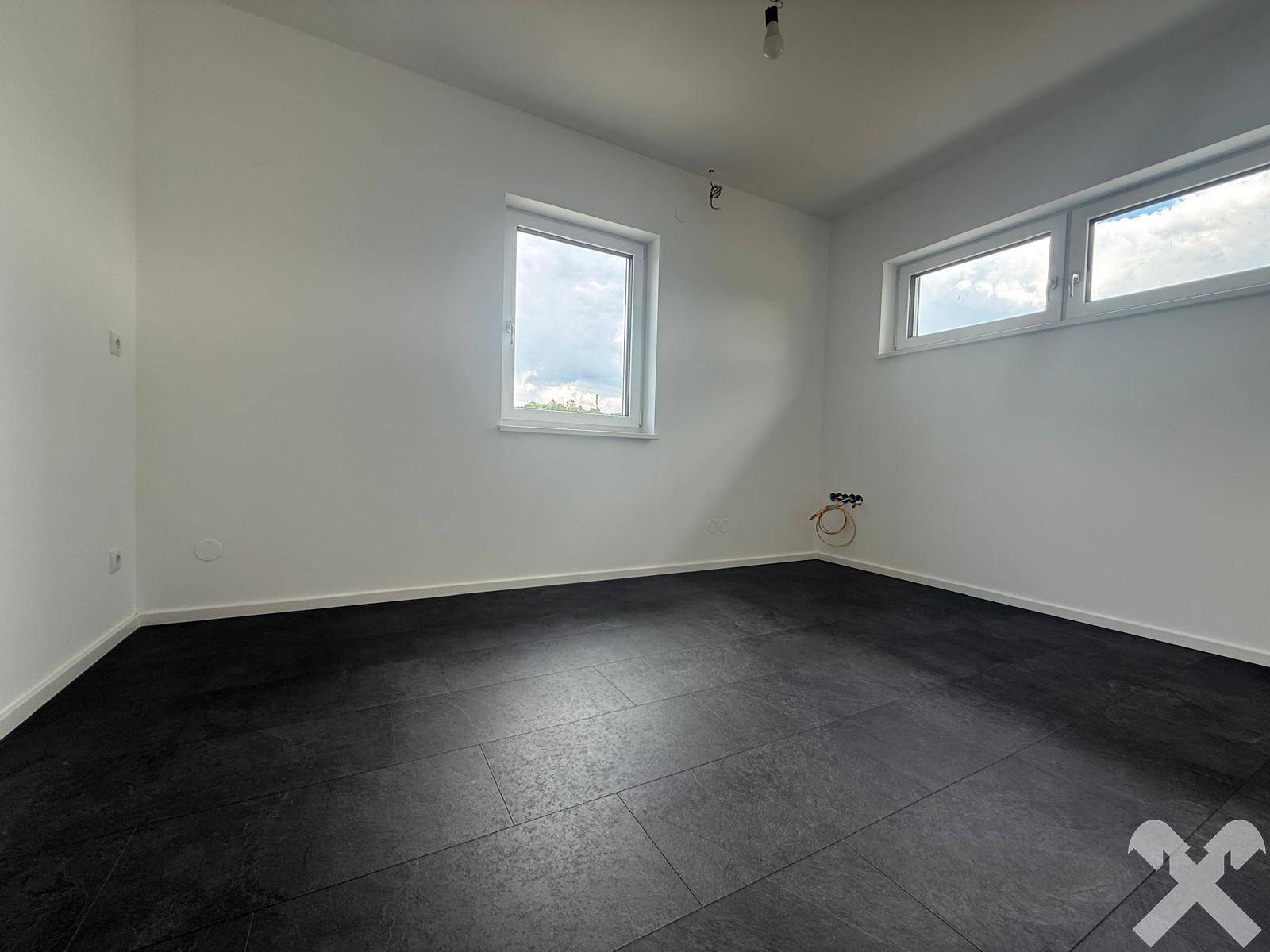 Helles Schlafzimmer mit zwei Fenstern und dunklem Fliesenboden, bereit zur Einrichtung.