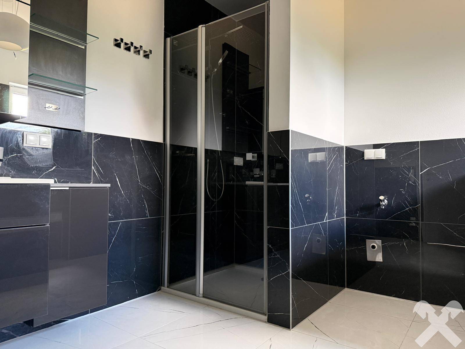 Modernes Badezimmer mit dunklen Marmorfliesen und geräumiger Duschkabine.