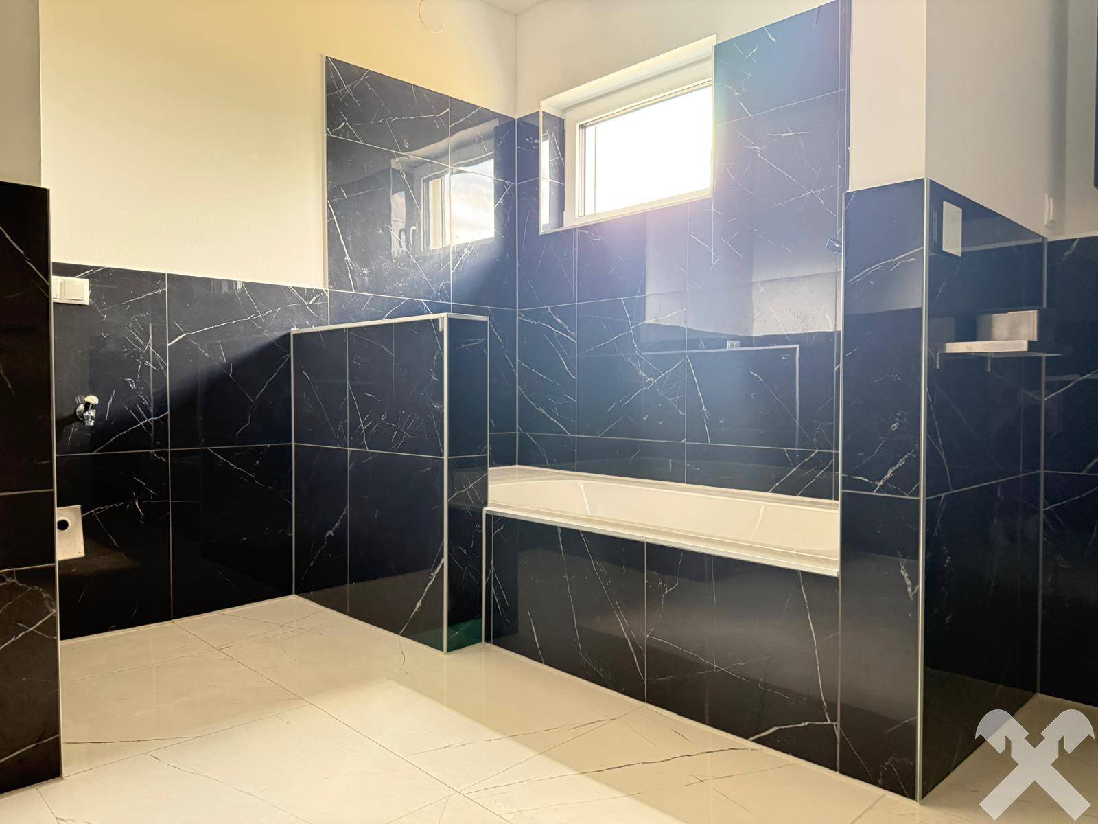 Modernes Badezimmer mit dunklen Marmorfliesen, Fenster und vorbereitetem Duschbereich.