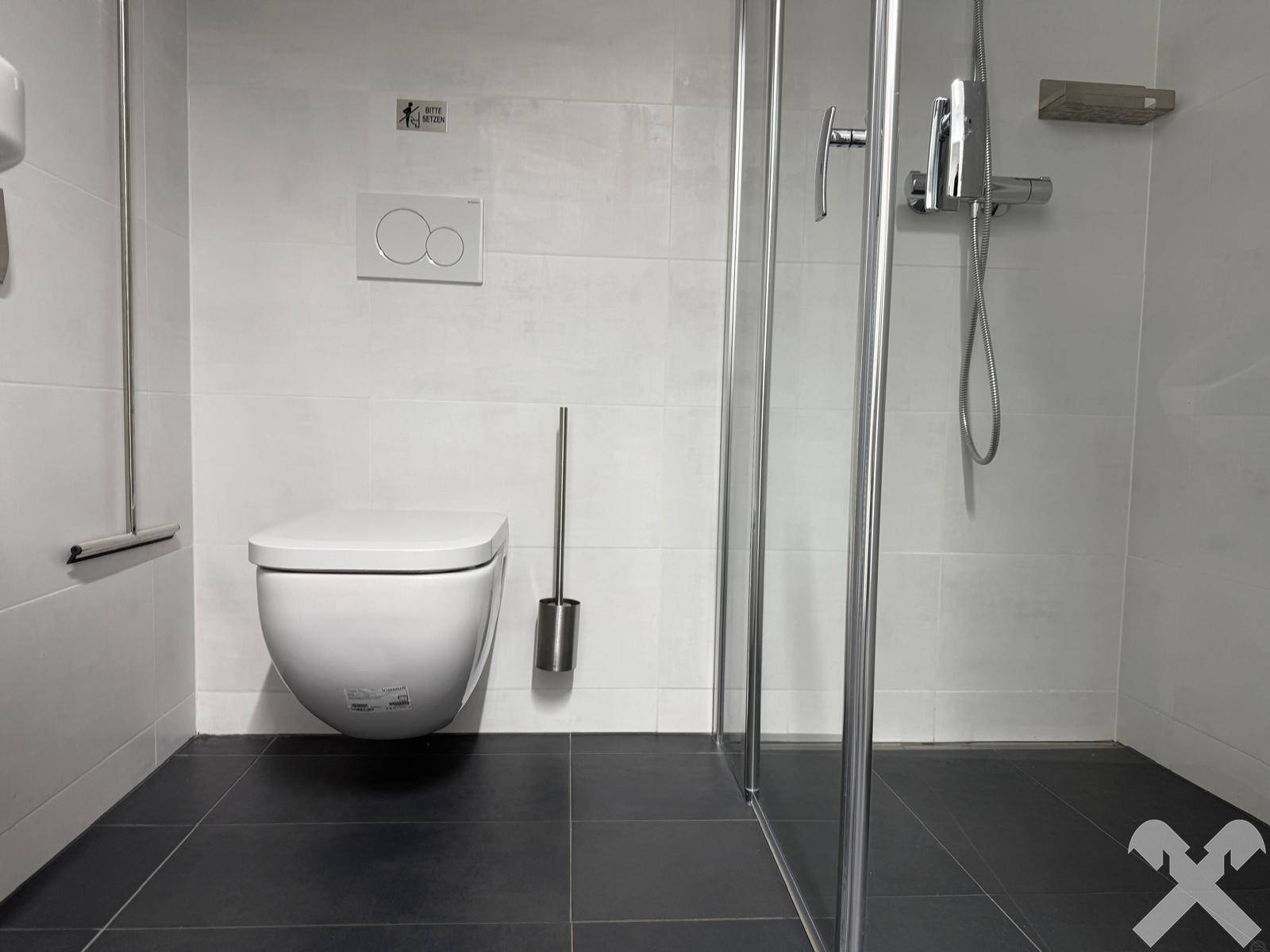Modernes Badezimmer mit weißem Fliesenboden, wandhängender Toilette und Duschkabine.