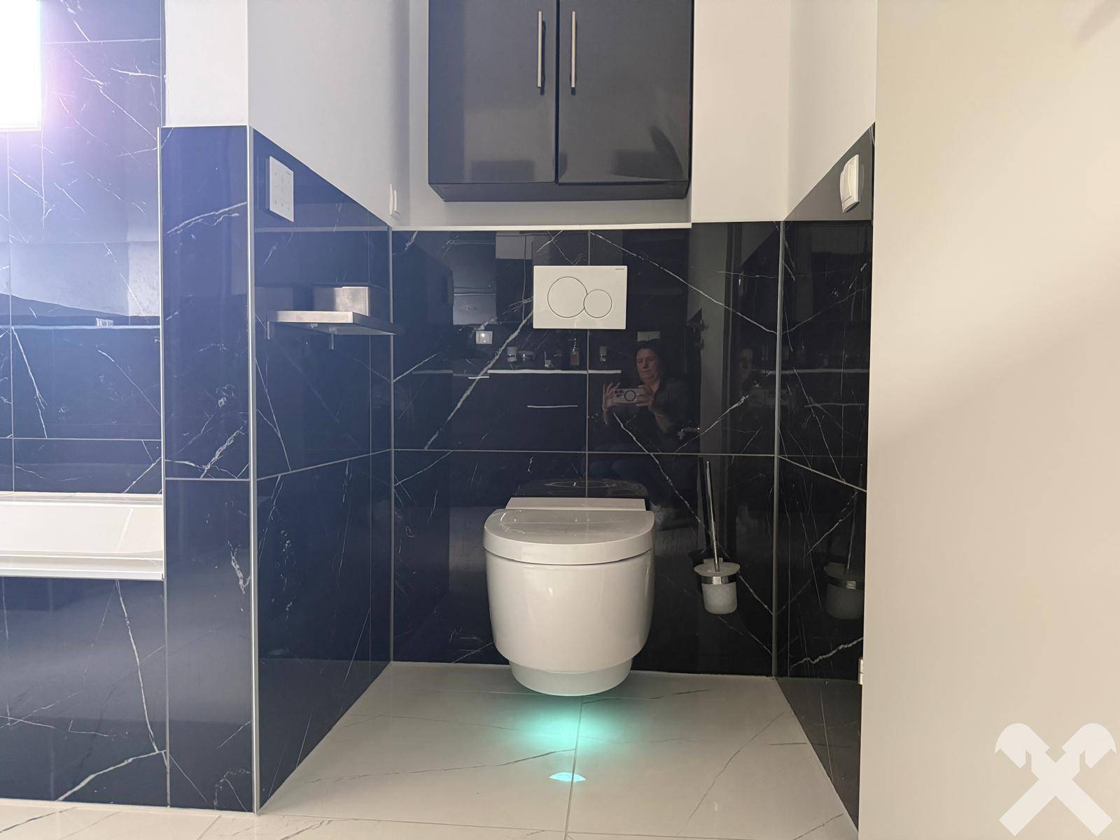 Elegantes Badezimmer mit dunklen Marmorfliesen und wandhängender Toilette mit Unterbodenbeleuchtung.