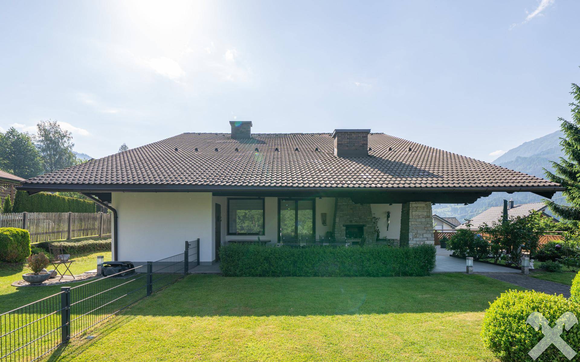 Rückseite des Hauses mit weitläufigem Garten, überdachter Terrasse und Blick auf die umliegende Natur.