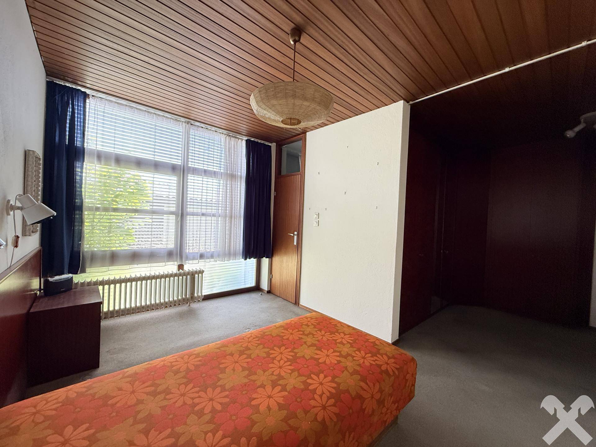 Schlafzimmer mit Holzboden, Holzdecke und großem Fenster, das viel Helligkeit bietet.