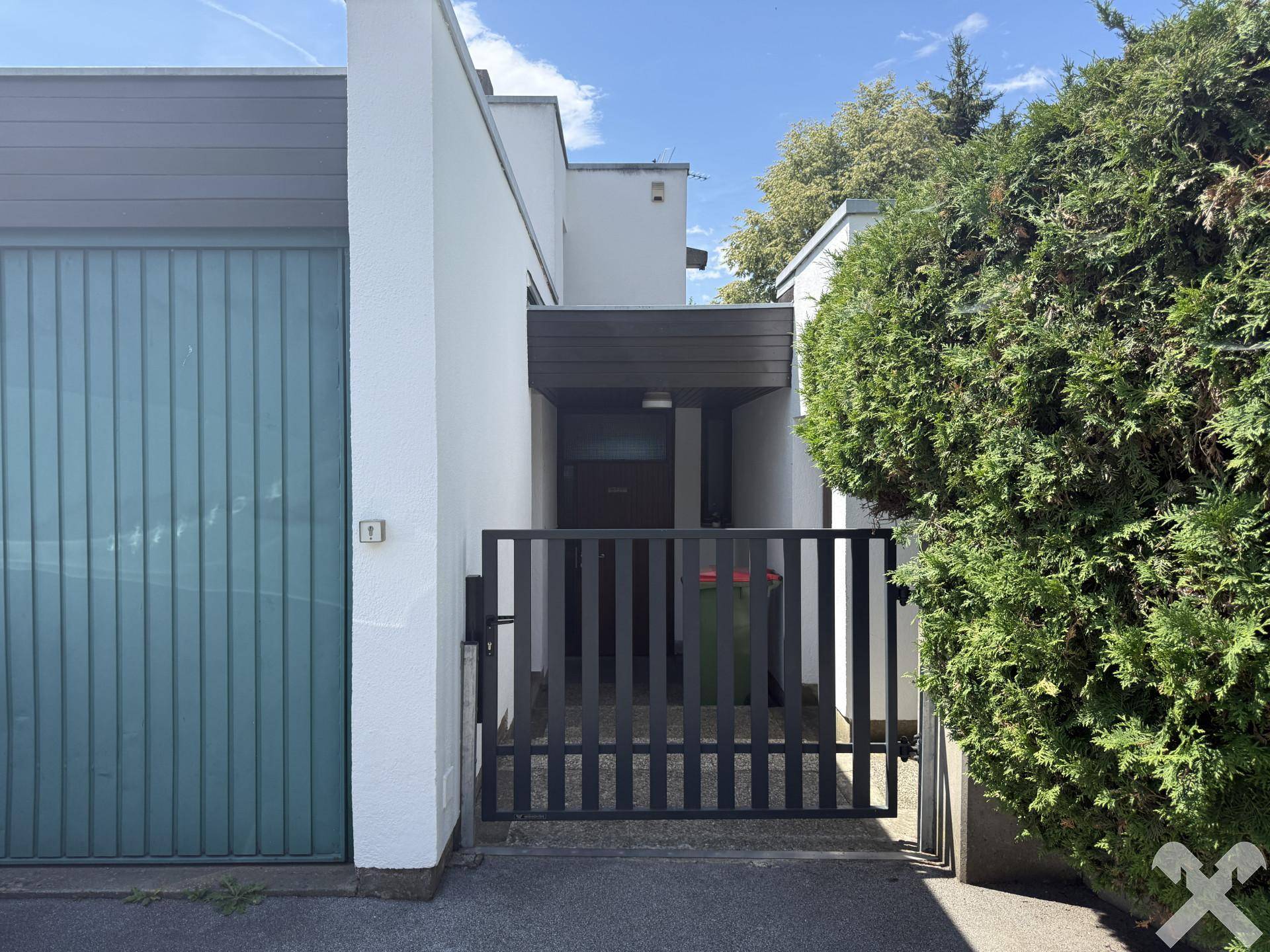 Eingangsbereich des Hauses mit Garage, Zaun und gepflegter Hecke im Vorgarten.