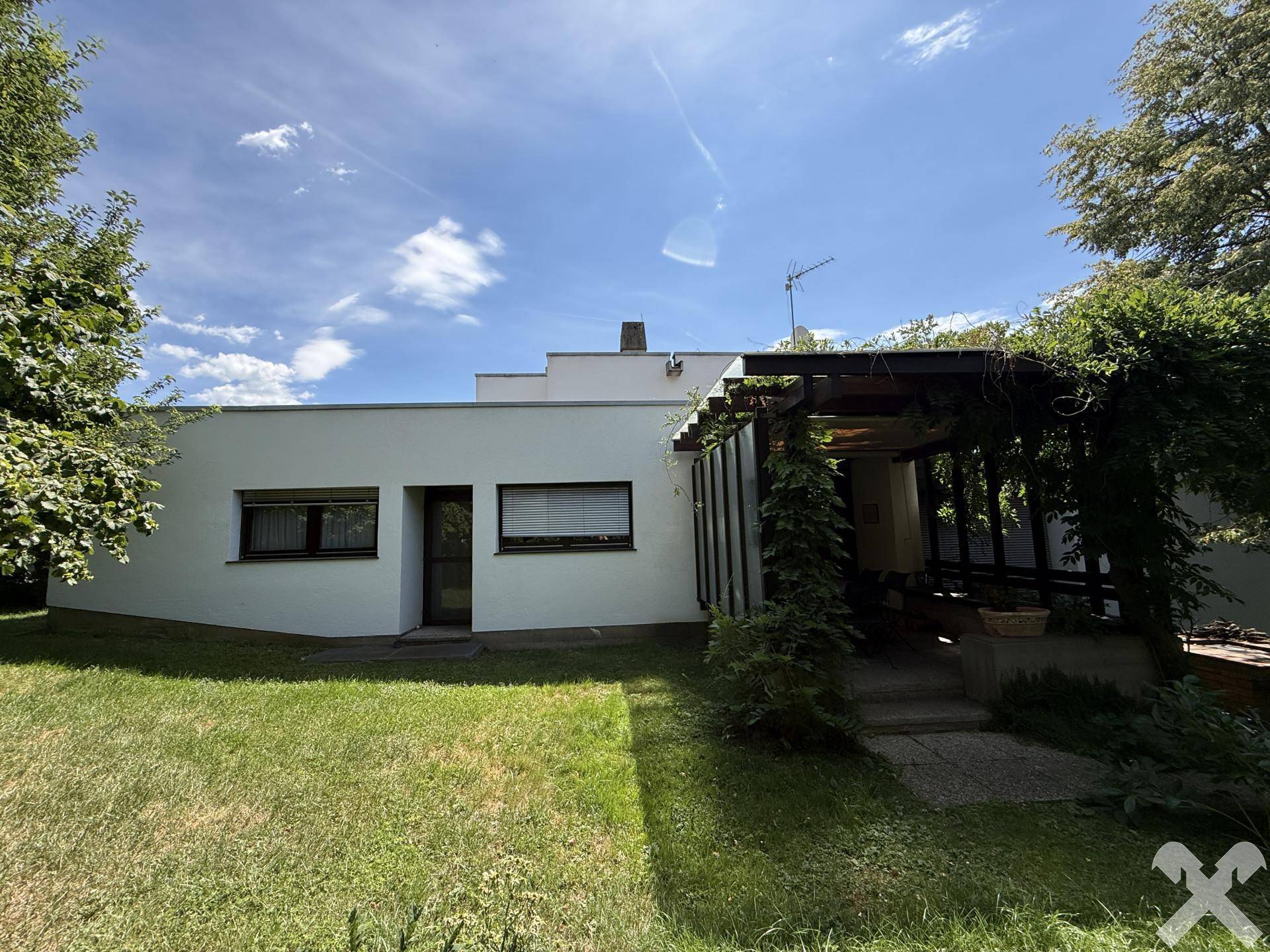 Moderne Hausfassade mit Flachdach und grüner Rasenfläche im Vordergrund unter blauem Himmel.