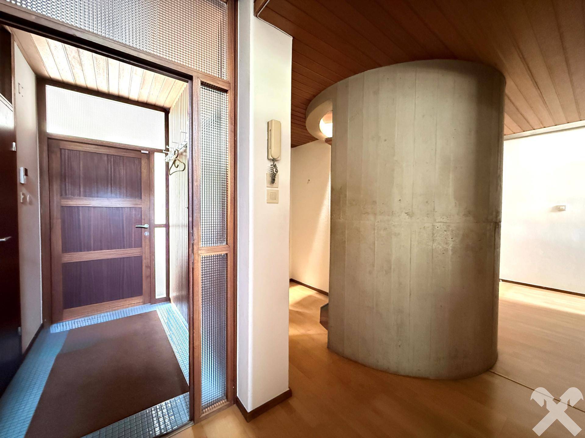 Heller Eingangsbereich mit Holzboden und einer markanten runden Betonsäule als architektonisches Element.