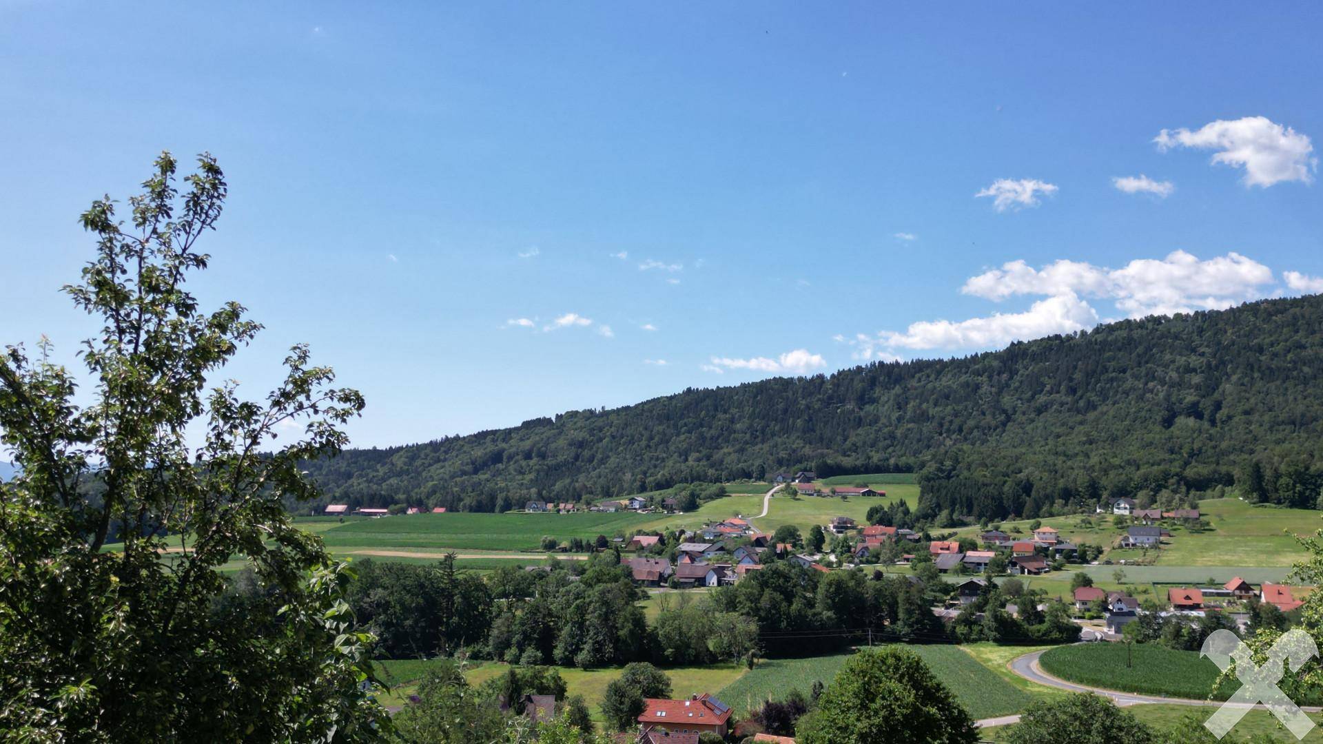 Panoramablick auf die hügelige, bewaldete Landschaft mit verstreuten Häusern unter blauem Himmel.