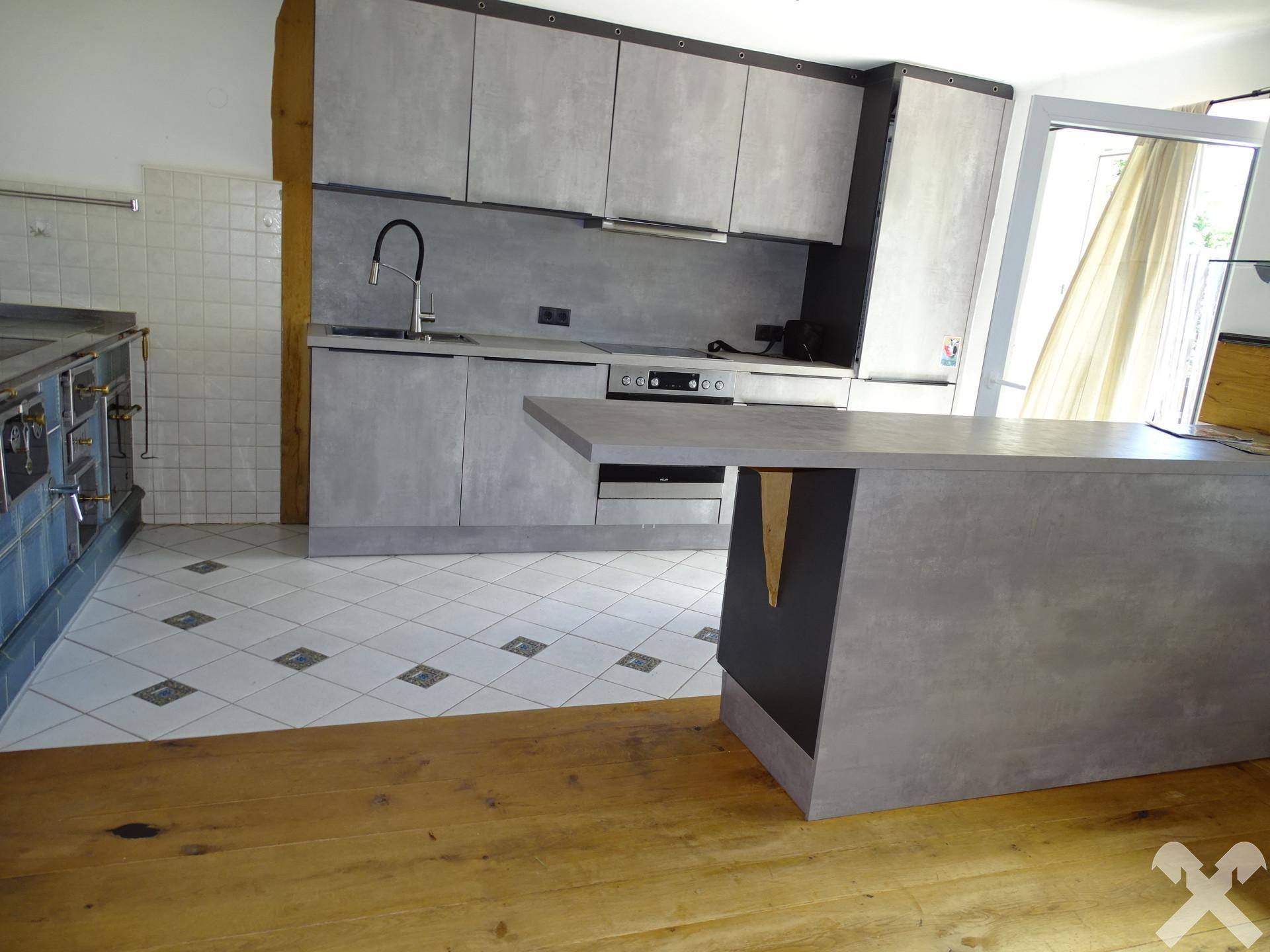 Moderne Küche mit grauen Schränken, einer Kücheninsel und einem traditionellen Kachelofen im Hintergrund.