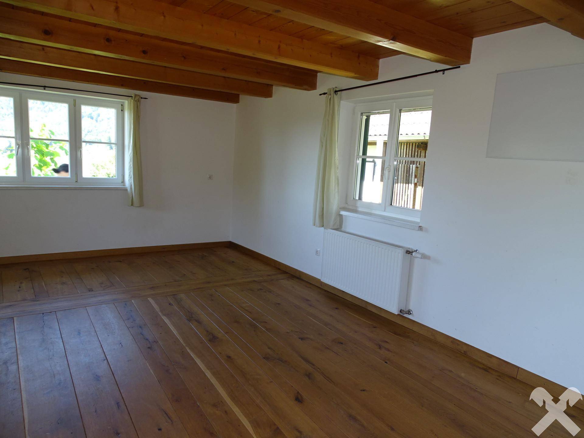 Helles Zimmer mit sichtbaren Holzbalken an der Decke und breiten Dielenböden.
