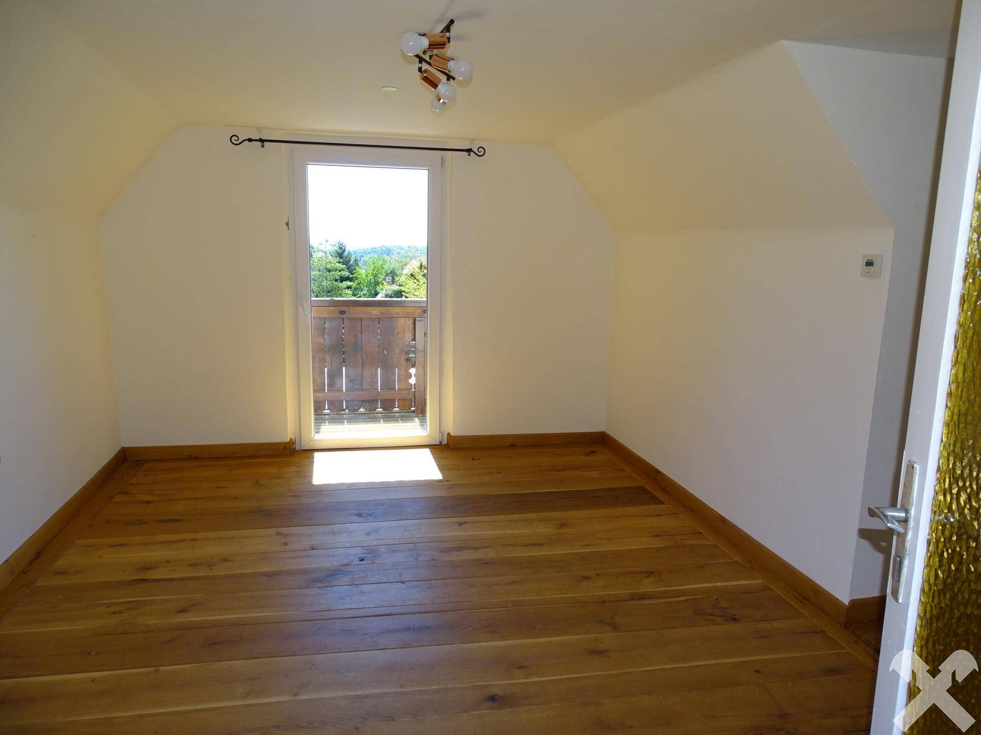 Schlafzimmer im Dachgeschoss mit Holzboden und Zugang zu einem kleinen Balkon.