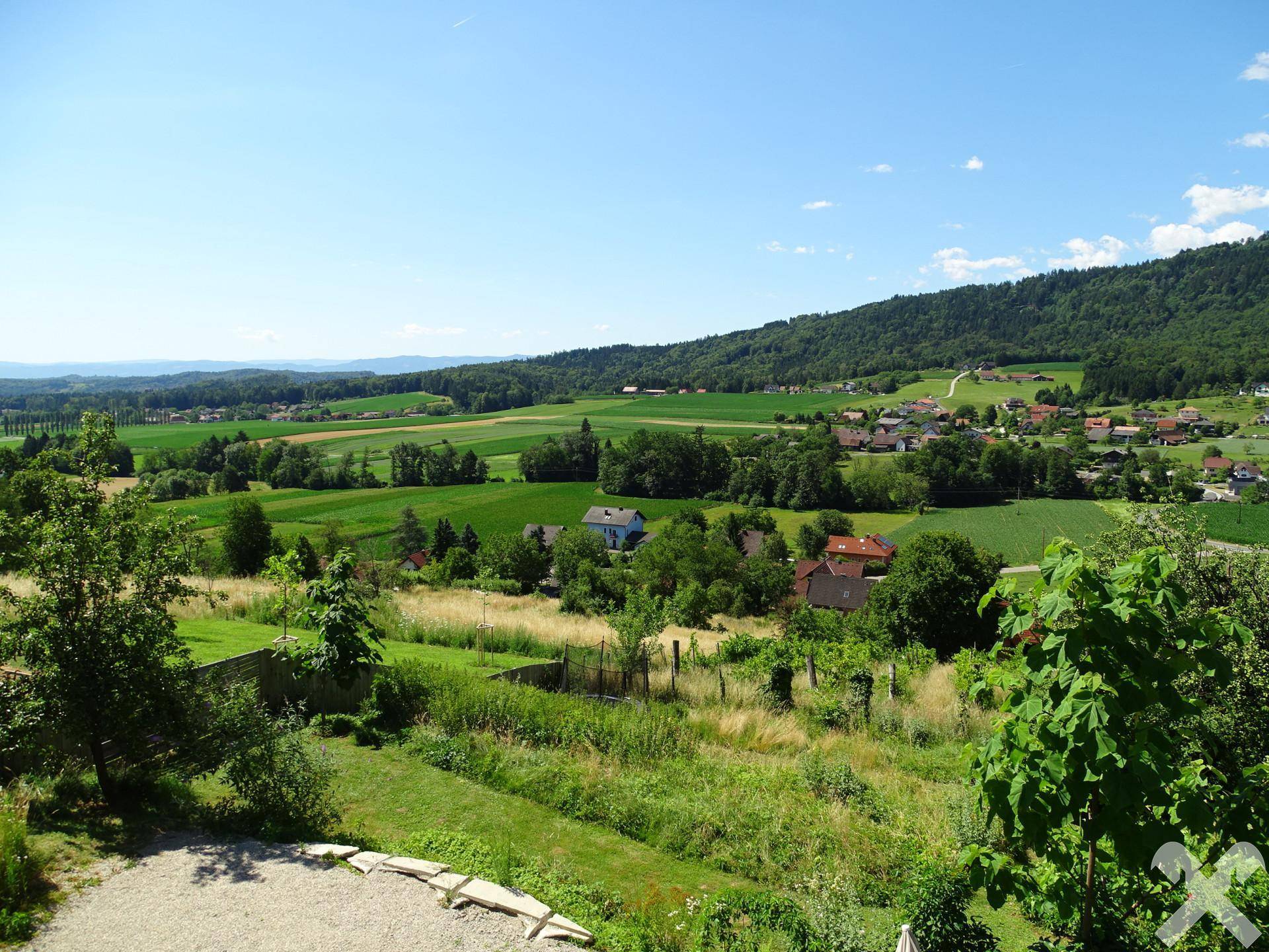 Weitläufiger Ausblick auf die grüne Landschaft mit Feldern, Wäldern und einem Dorf in der Ferne.