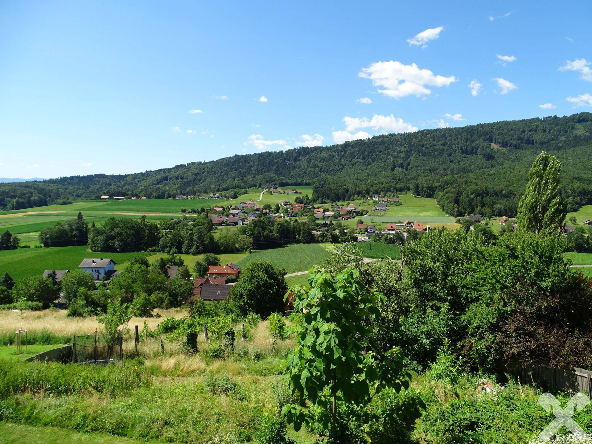 Panoramablick über die idyllische, hügelige Landschaft mit üppigem Grün und blauem Himmel.