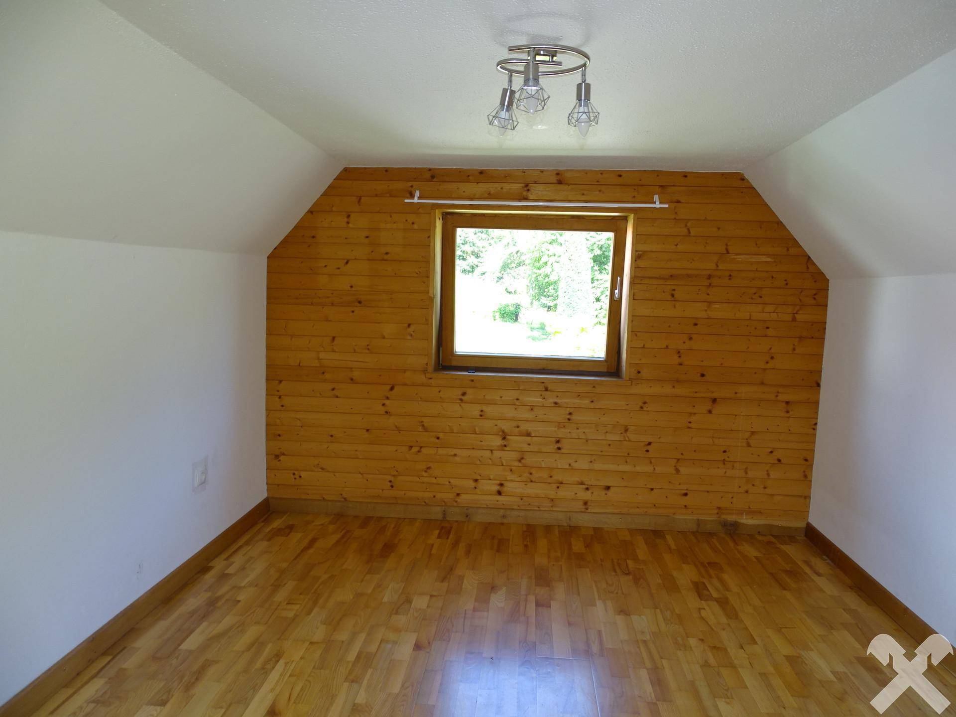 Gemütliches Dachzimmer mit Holzvertäfelung an einer Wand und hellem Holzboden.